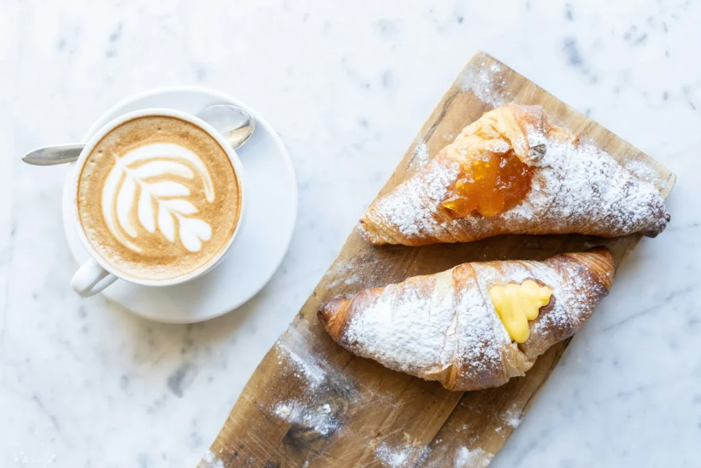 A steaming cappuccino served alongside a freshly baked croissant on a rustic wooden table.