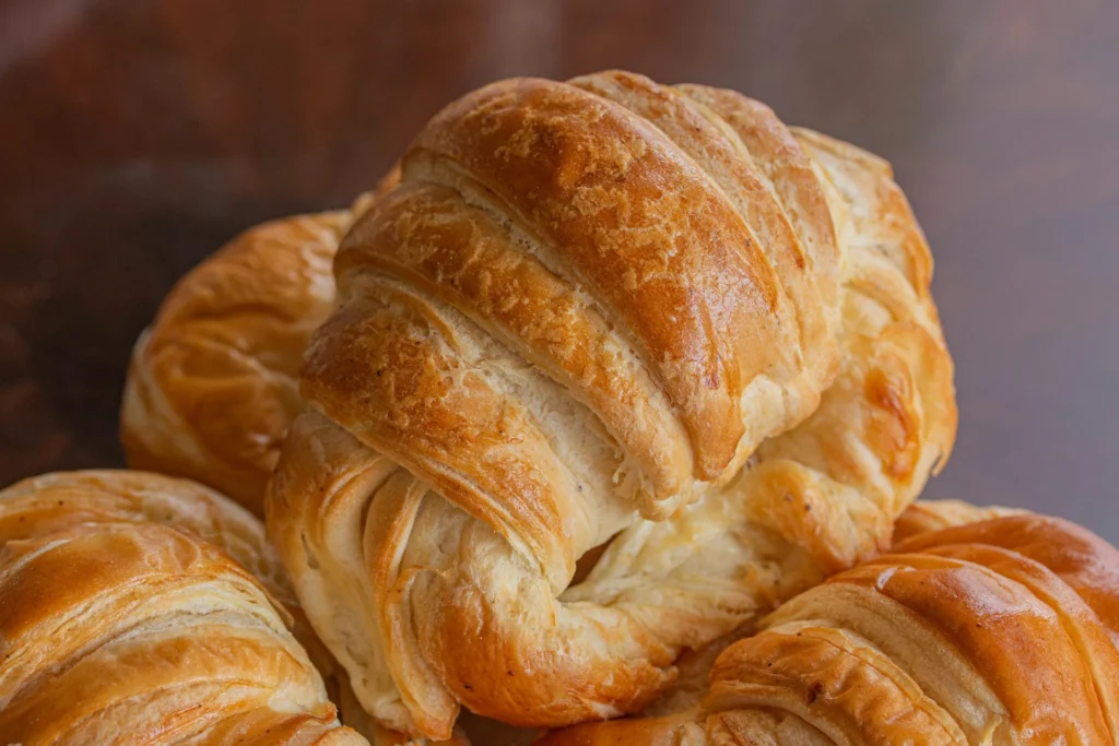 A plate of freshly baked croissants with a golden, flaky crust, displayed on a wooden table.