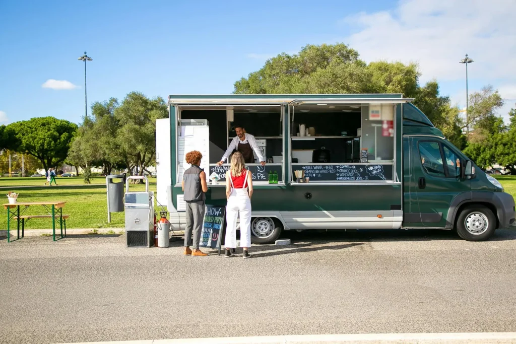 A colorful food truck with a serving window open, offering a variety of street food in a city setting.