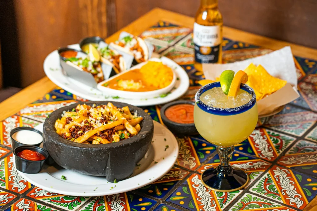 A colorful Mexican food spread with tacos, guacamole, and salsa on a wooden table.