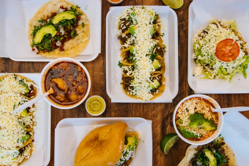 A vibrant spread of traditional Mexican foods, including tacos, guacamole, and chiles rellenos, on a colorful tablecloth.
