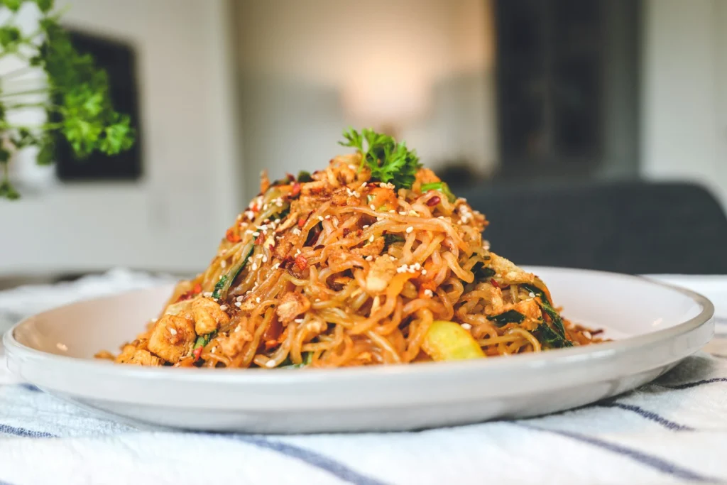 A plate of Pad Thai, a traditional Thai noodle dishes, garnished with lime, peanuts, and fresh herbs.