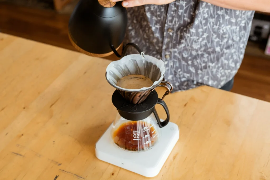 A barista pouring hot water over a coffee dripper to make pour-over coffee.