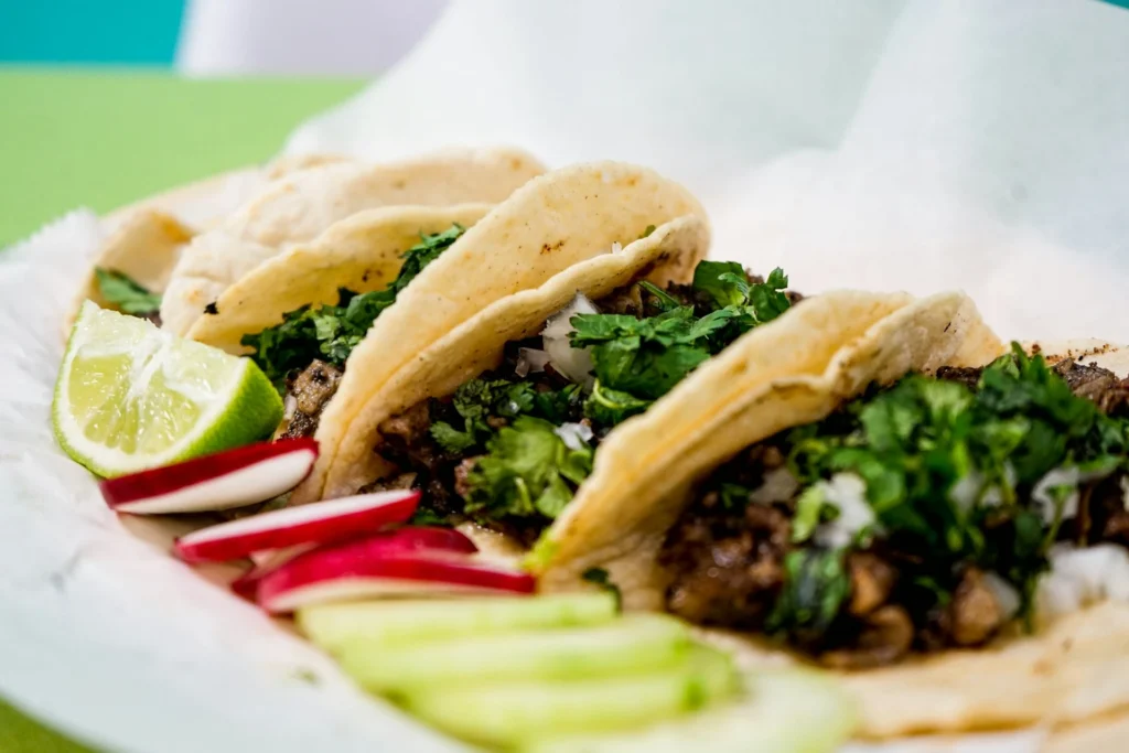 A plate of traditional Mexican tacos dishes with various fillings, garnished with fresh cilantro and lime wedges.