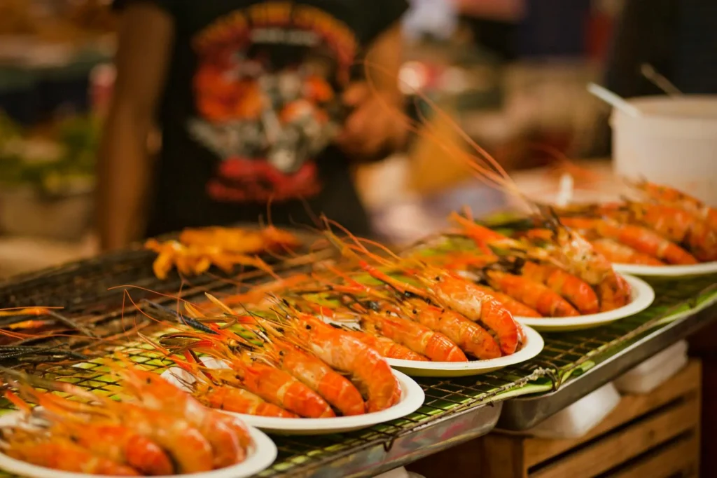 A lively Thailand street food scene with vendors preparing various dishes and a crowd of people.