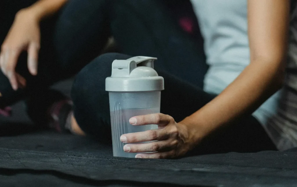 A person refilling a water bottle from a water fountain in a gym, illustrating the importance of hydration during exercise.